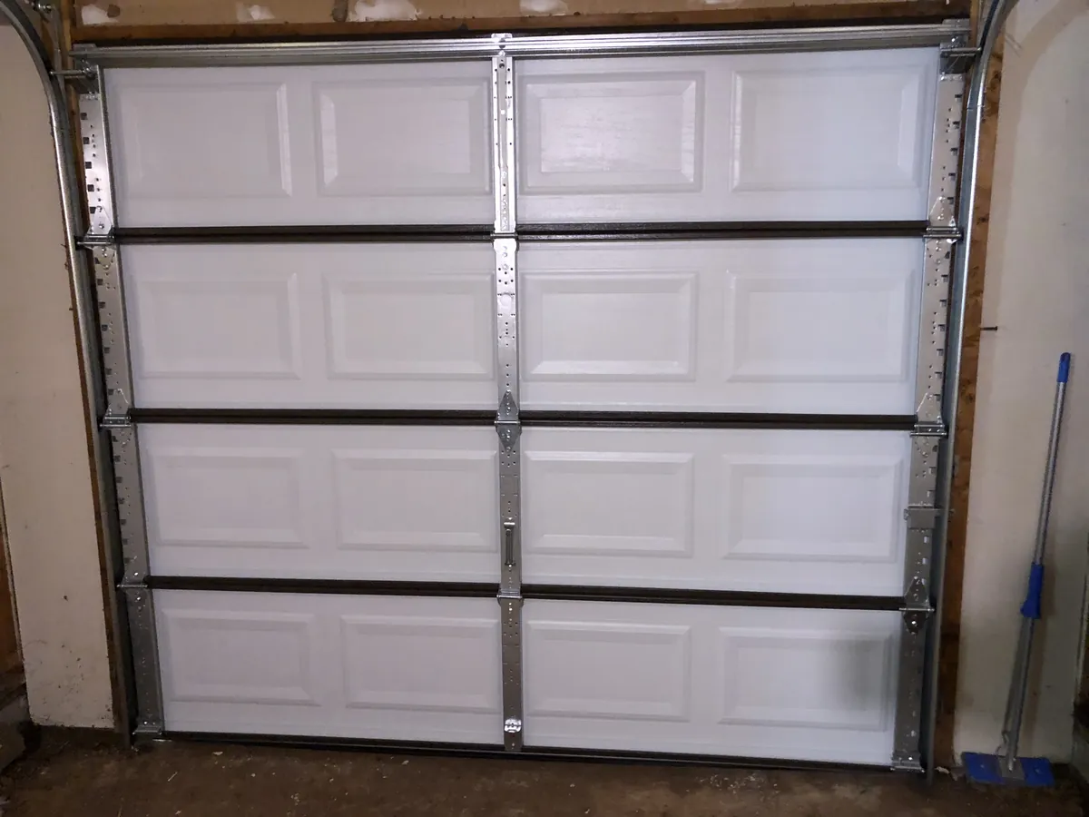 Interior view of a white paneled sectional garage door with steel hardware